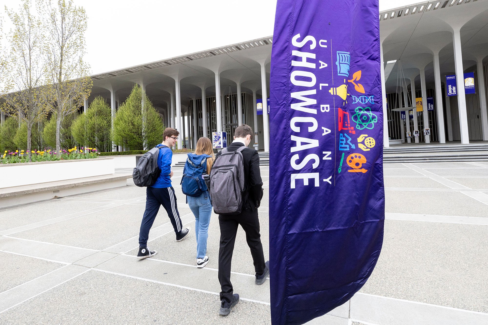 Students walk by a purplbe sign outdoors that says UAlbany Showcase.