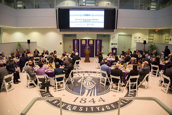 Event photo from the President's Breakfast showing 80 participants seated in the atrium of University Hall. President Havidán Rodríguez is speaking at podium.  