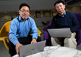 UAlbany atmospheric scientists Aiguo Dai and Fangqun Yu sit with laptops in the University Hall atrium.