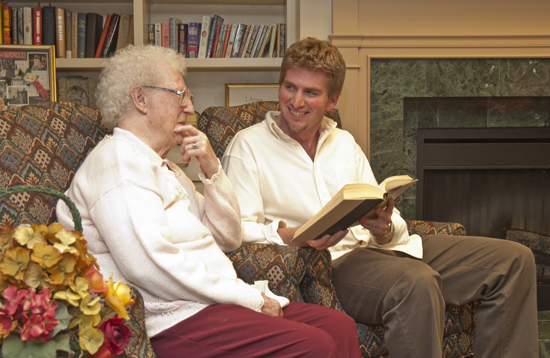 College student reading a book to an older person.