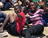 Two Haitian chidren, sitting on the ground, smile and give thumbs-up to the cameraman
