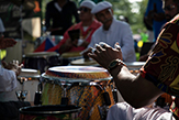 Hands come down upon the conga drum by a player just outside the right frame