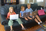 Three children study with laptops while sititing on a home couch