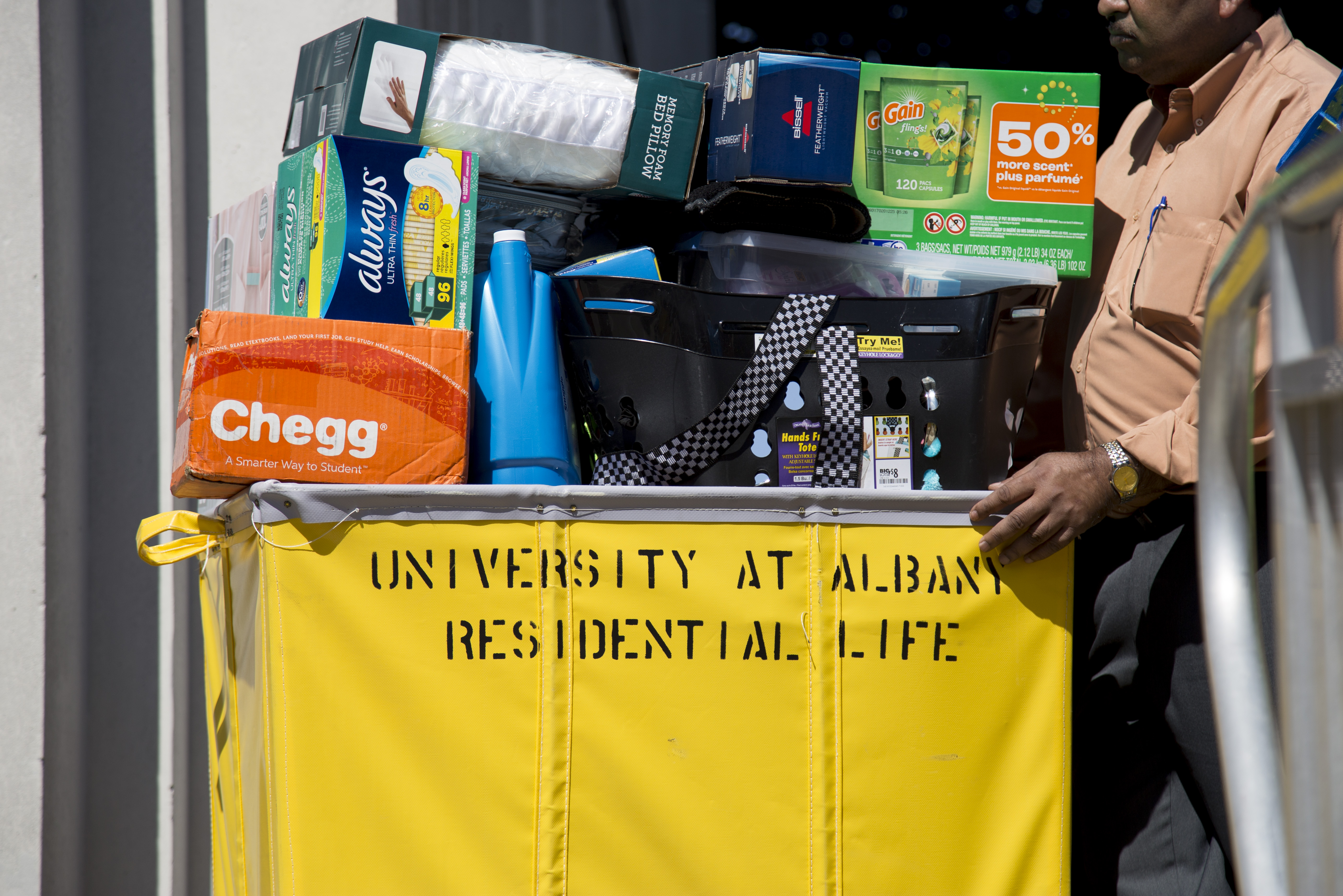 A man pushes a yellow rolling bin labeled "University at Albany Residential Life" that is full of a student's belongings