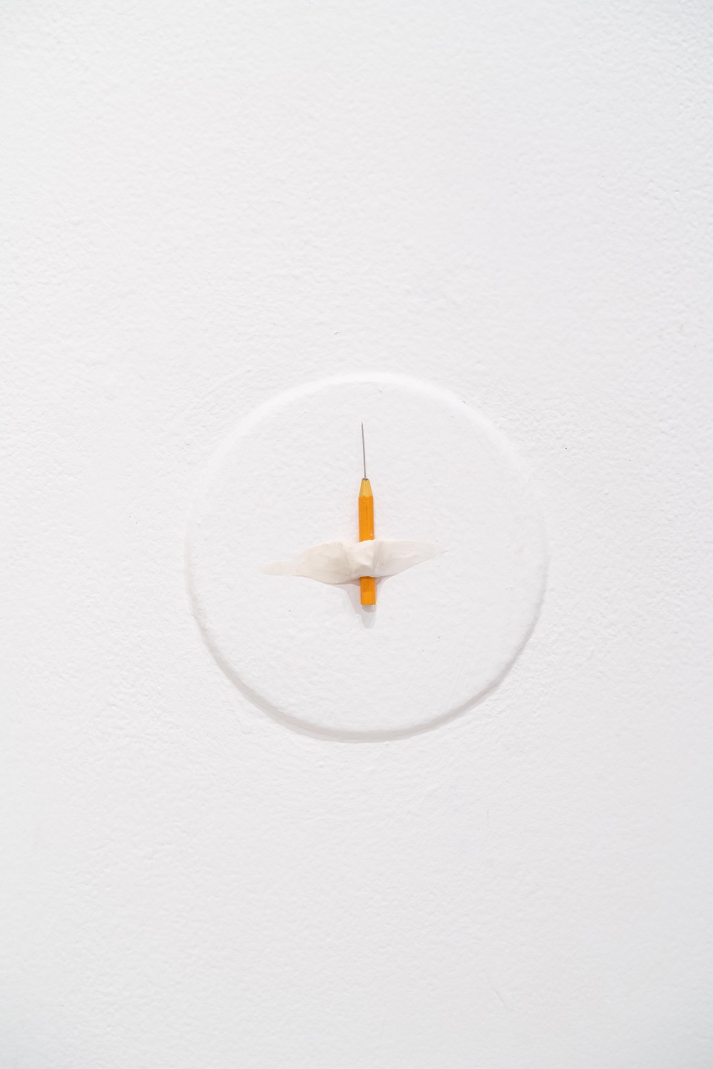 A short pencil with a long lead tip is taped to a white wall