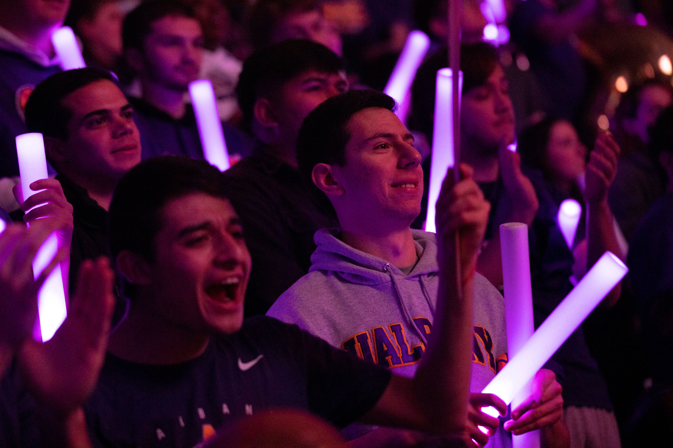 Students hold purple glow sticks as they stand and cheer for a UAlbany team.