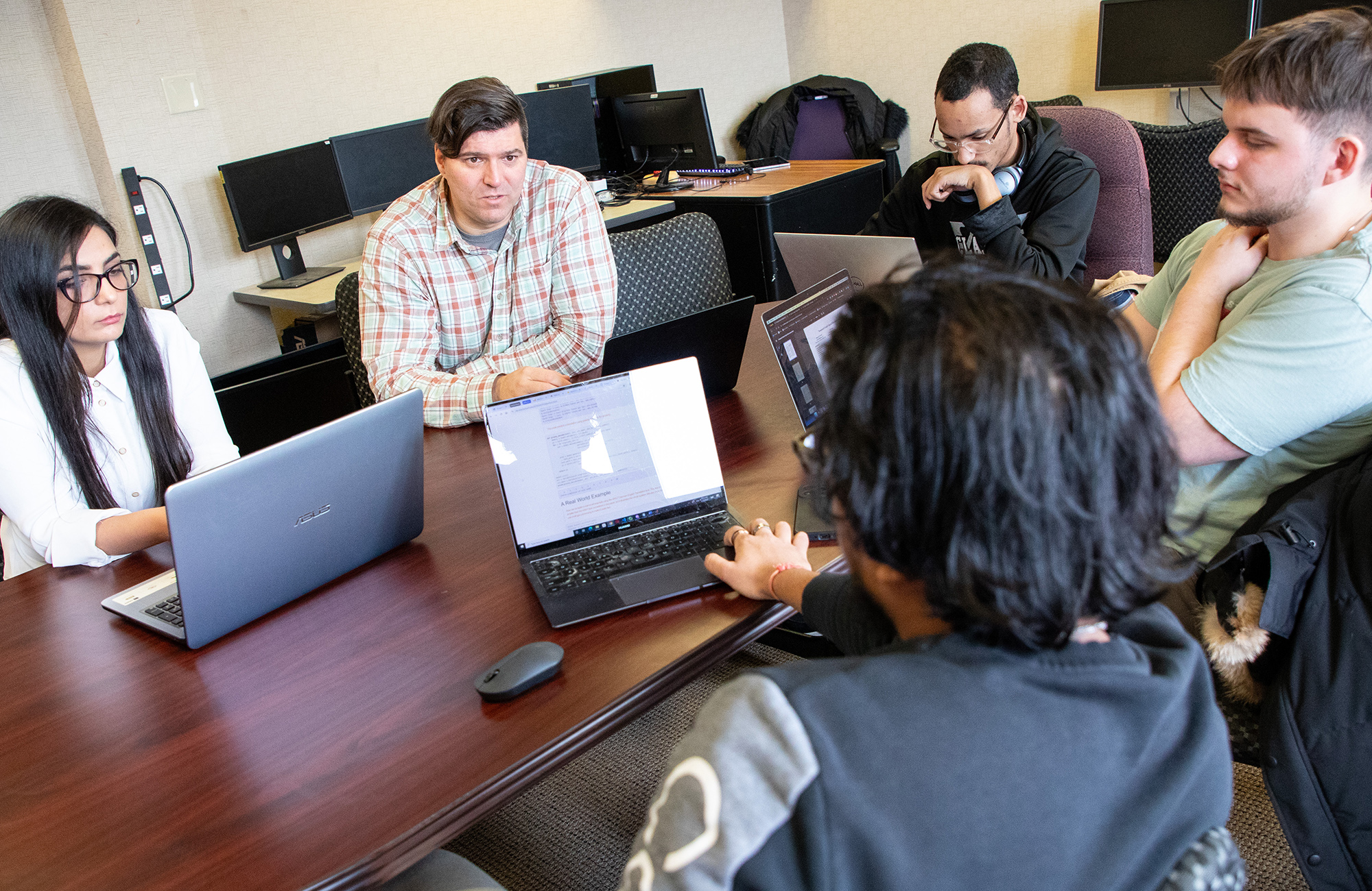 UAlbany computer scientist Petko Bogdanov meets with students at a desk in his computer lab, with students looking at their laptops.