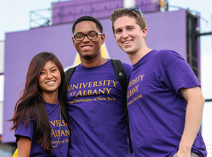 Three UAlbany students in purple t-shirts pose for a photo