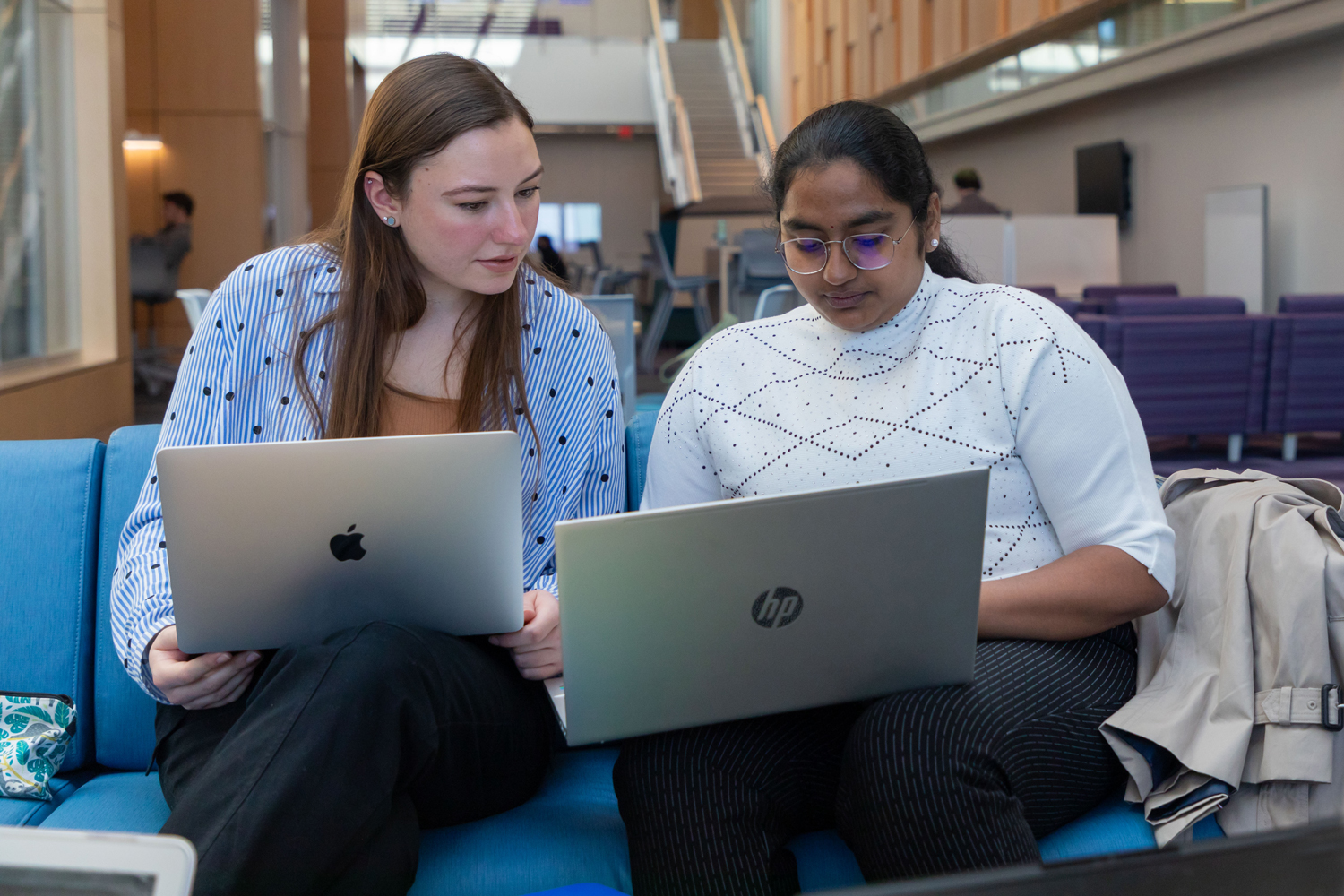 Two students sitting on a couch with laptops.