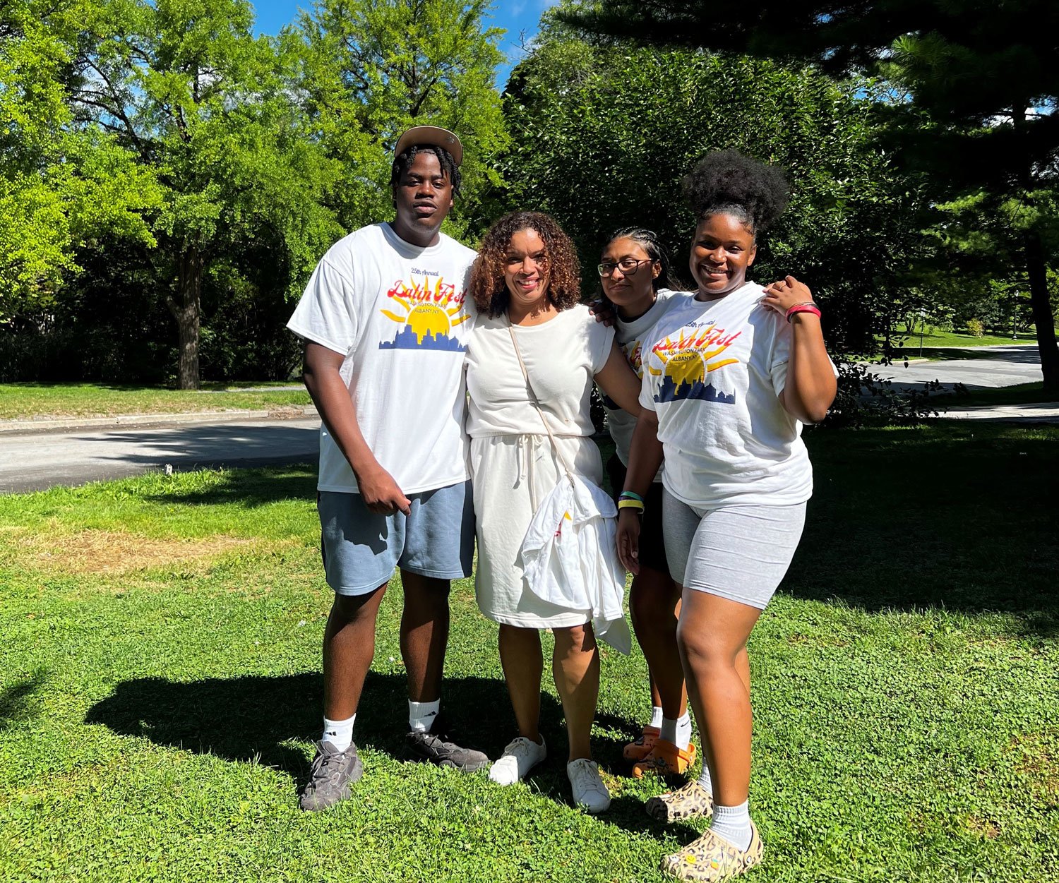 Three students wearing white 2022 LatinFest t-shirts pose with a woman in a white dress.