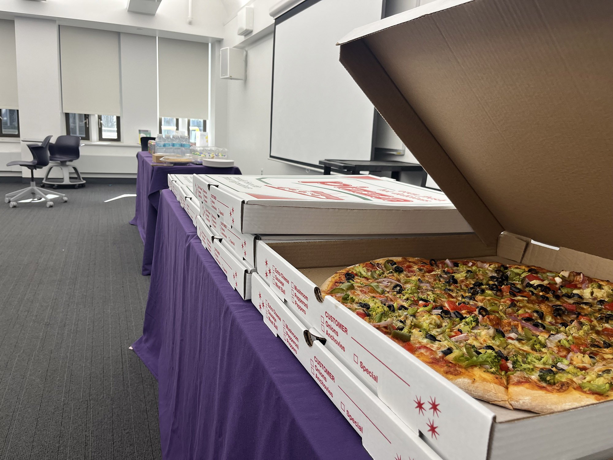 several boxes of pizza are on a table with a purple table skirt.