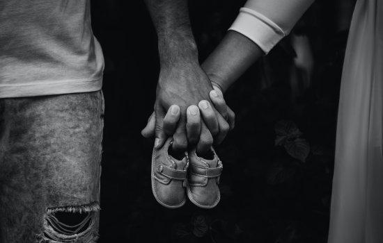 Two parents hold hands and a pair of baby shoes.