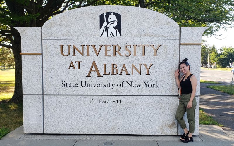UAlbany Master of Social Work student and Graduate Ambassador Yumeno Nagata posing in front of a University at Albany sign.