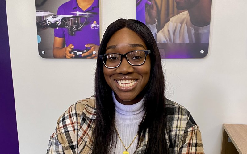 Maimouna Camara, a UAlbany MSW student, sits at a desk and smiles.