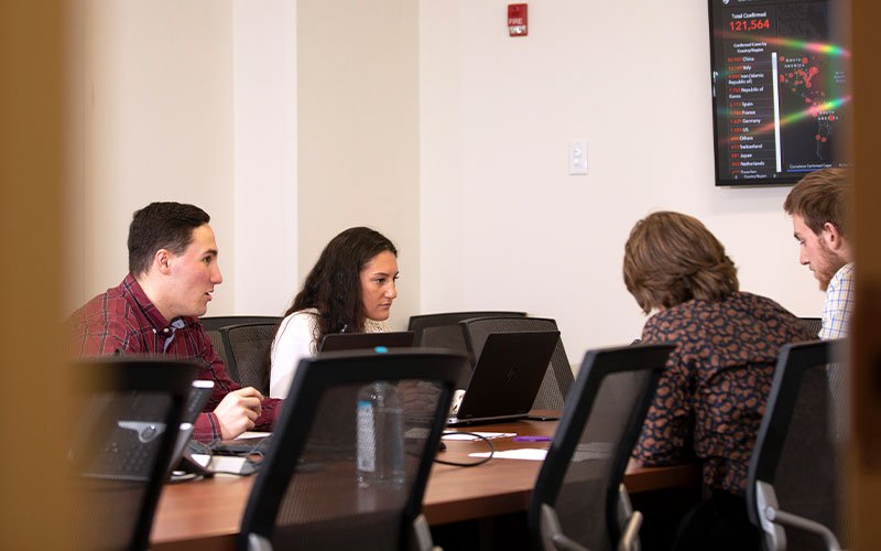 Fours students sit around a table and interact with technology as a part of UAlbany's Virtual Operations Support Team (VOST)