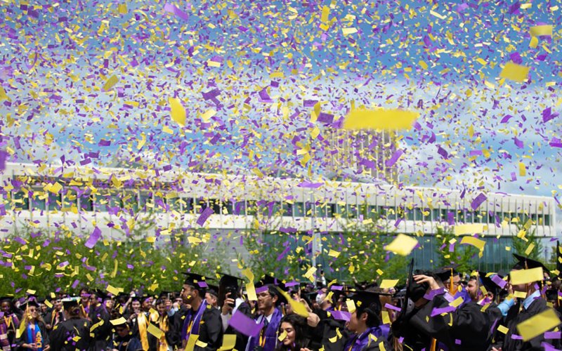 Purple and gold confetti fills the air as students dressed in commencement gowns celebrate graduation on Collins Circle at the University at Albany.