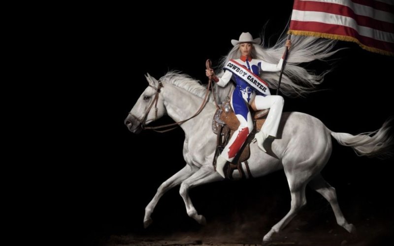 Beyonce rides side-saddle on a white horse, carrying an American flag and dressed in red, white and blue cowboy-inspired garb