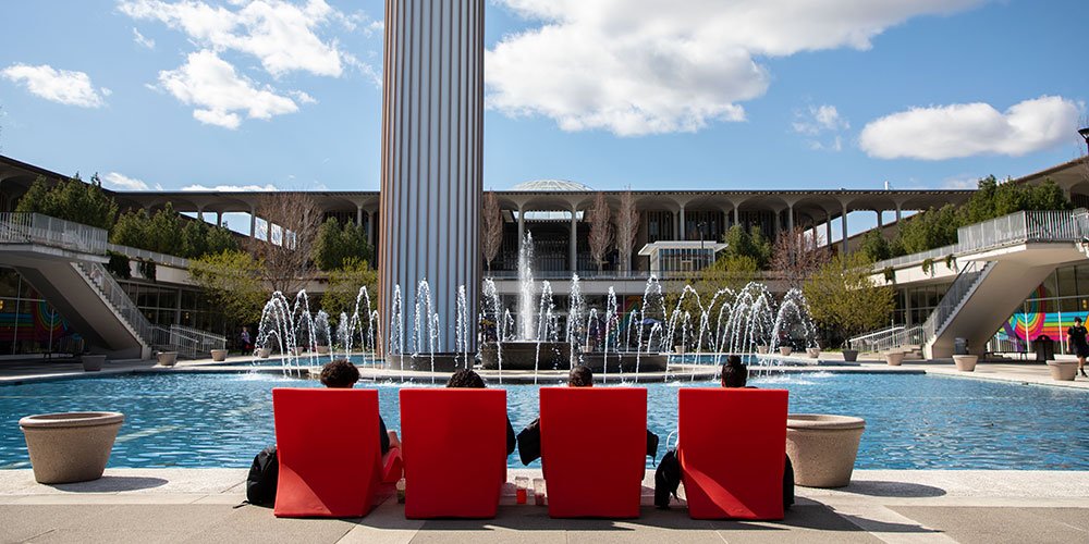 Students sitting in red chairs by the main fountain.