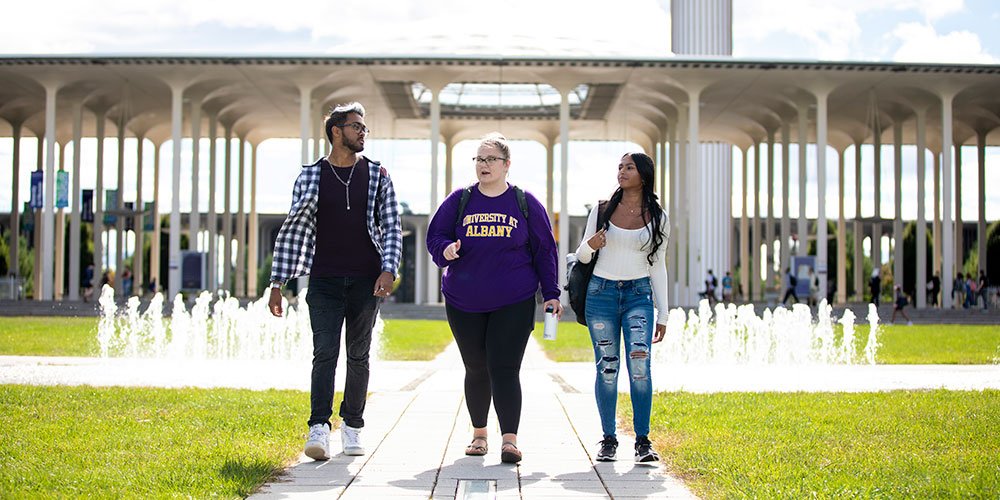 Three students walking through the entrance fountain on campus.