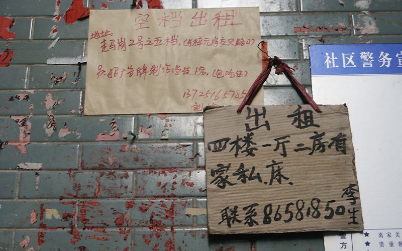 Handwritten signs hang on a faded and chipped wall of green tile, advertising rooms for rent in China