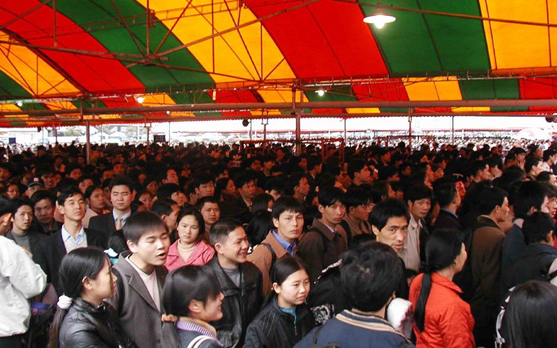 A crowd of people are packed beneath a red, teal and yellow awning outside of Guangzhou Station in China.