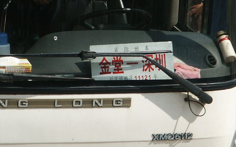 The dashboard of a white shuttle bus. A sign in the window visible behind the windshield wiper, displays Chinese text that translates to: "Jin Tang Yi Shenzhen." 