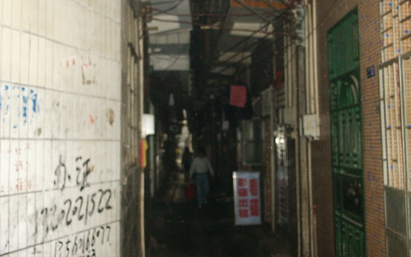A person walks through an out-of-focus dark alley in China.