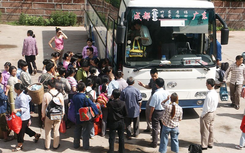 A crowd of people waits by a shuttlebus in China as a man with a yellow bag walks off the bus.
