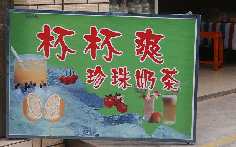 A sign displays an advertisement for Pearl Milk Tea written in red Chinese lettering on a green backdrop. A refreshing looking image of the tea is displayed next to the text.