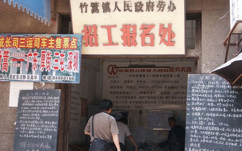 A man walks into a labor office in China. All around the entrance, signs written in Chinese promote work and labor recruitment.