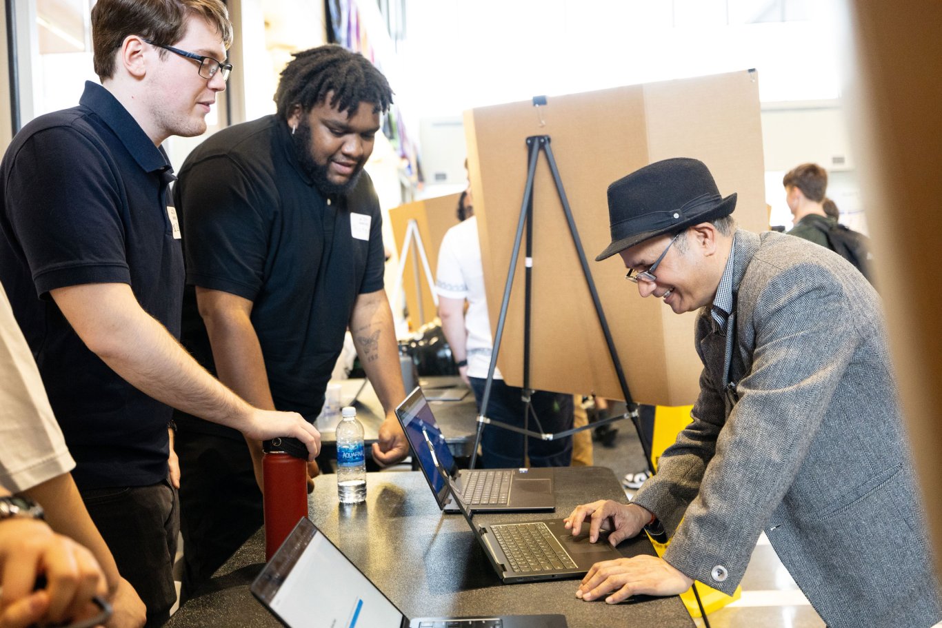 Two students demonstrate something on a laptop as a Showcase Day attendee looks on.