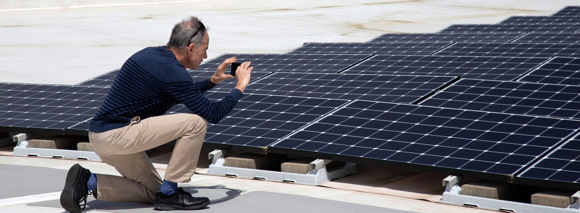 A professor kneels down to take a photo with his smartphone of a solar panel array