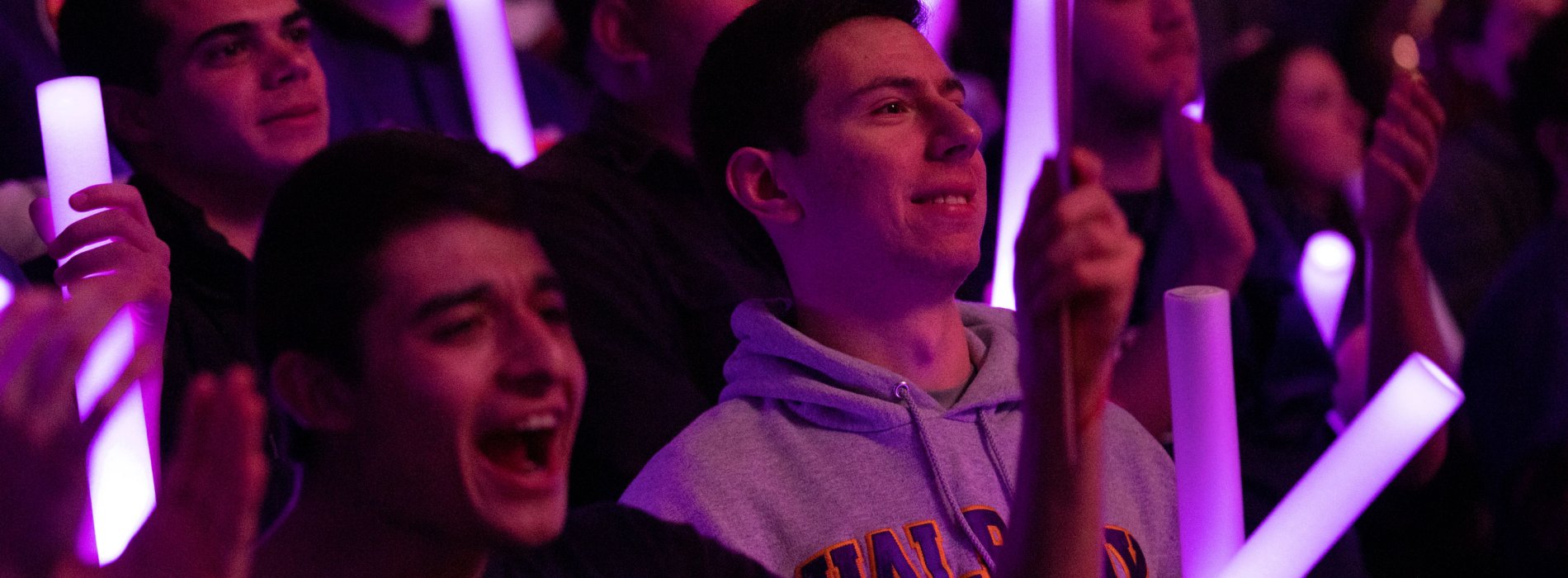 Students hold purple glow sticks as they stand and cheer for a UAlbany team.
