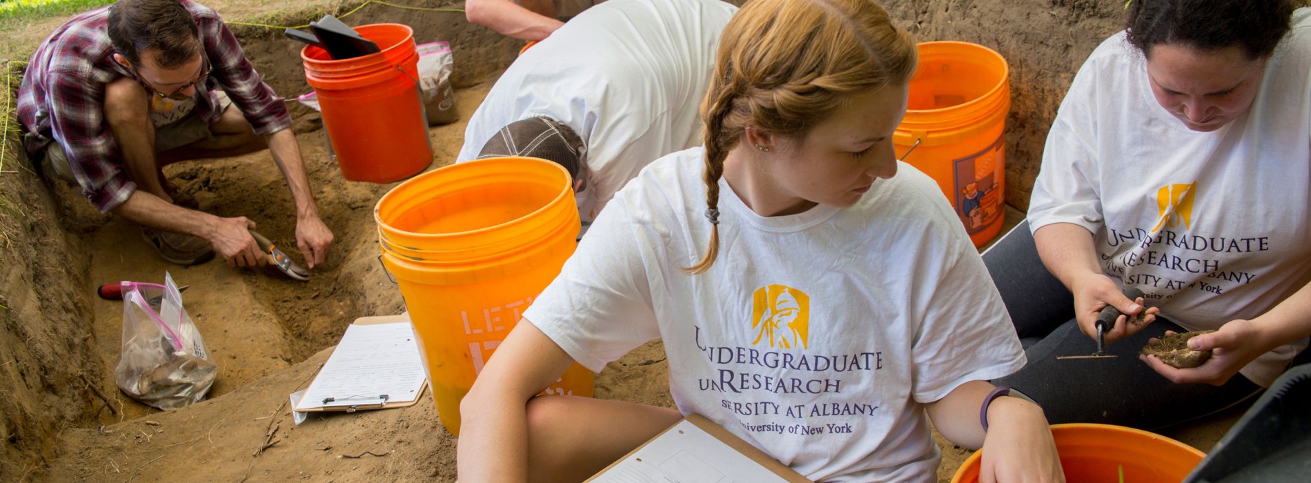 Five students wearing Undergraduate Research t-shirts excavate artifacts at the archaeology dig.