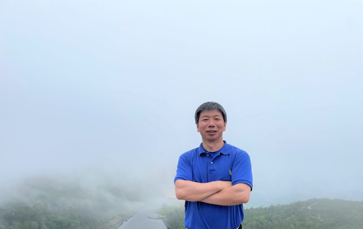 ASRC's Fangqun Yu stands in front of a foggy road in a blue polo with his arms crossed.