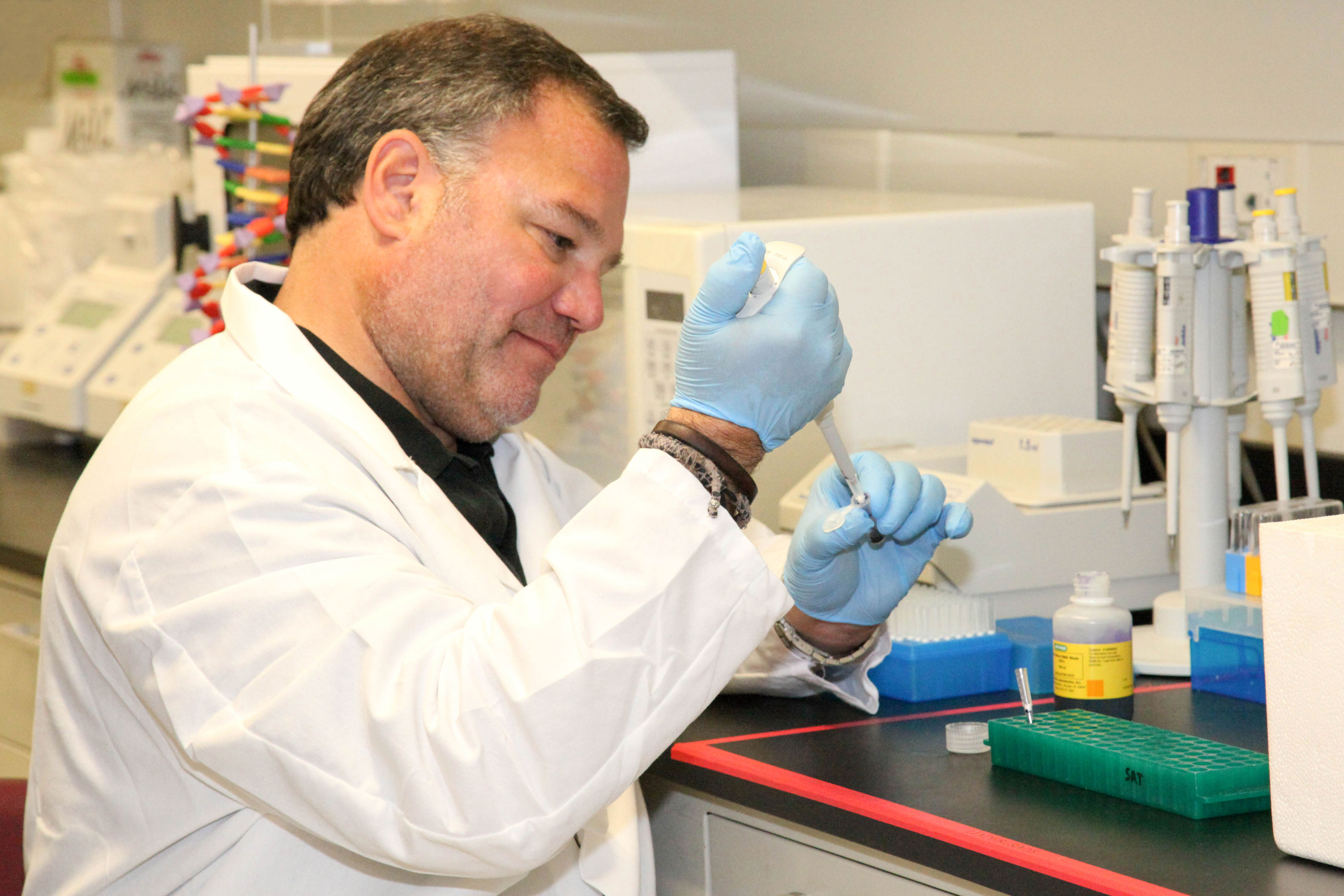 A researcher in a white lab coat and blue protective gloves uses an instrument inside a lab.