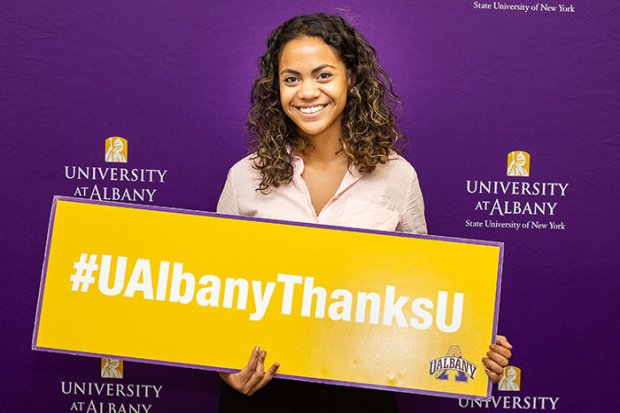 A UAlbany student holds a poster with the #UAlbanyThanksU hashtag