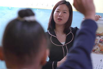 A teacher in the classroom; child raising hand to ask a question.
