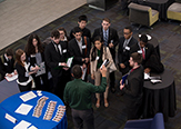 Eagle's eye view of the Massry Center of Business' living room. A group of business students listen to a corporate partner during a 'Cyber Week' job fair. 