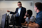 Photo of students seated at desktop computers, looking at Goel (standing in front of a whiteboard)