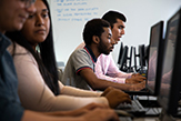 Side view of a row of students working at computers in a classroom.