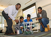 A STEP-affiliated staff member and three high school students demonstrate their STEM-based final project in a classroom. 