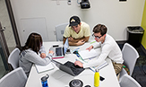 Photo of three students working at a table together on a project.