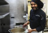 Chef Jude Jerome in a black shirt and chef's hat prepares a dish in the Calypso kitchen.