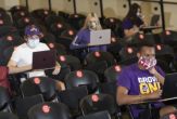 Students with face maskes sit in a lecture hall, with seats around them marked with Xes to enforce social distancing