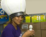 a woman wearing a light bulb hat holds a CFL bulb