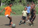 Five Hattian children play soccer on a dirt field.