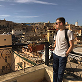 Student Dylan Marshall standing in front of balcony overlooking buildings in the Atlas Mountain Region of Morocco. 