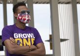 a student in a purple shirt and a facemask with hearts on it stands with his arms crossed