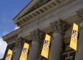 Yellow UAlbany banners hang from the pillars under the roof of Milne Hall